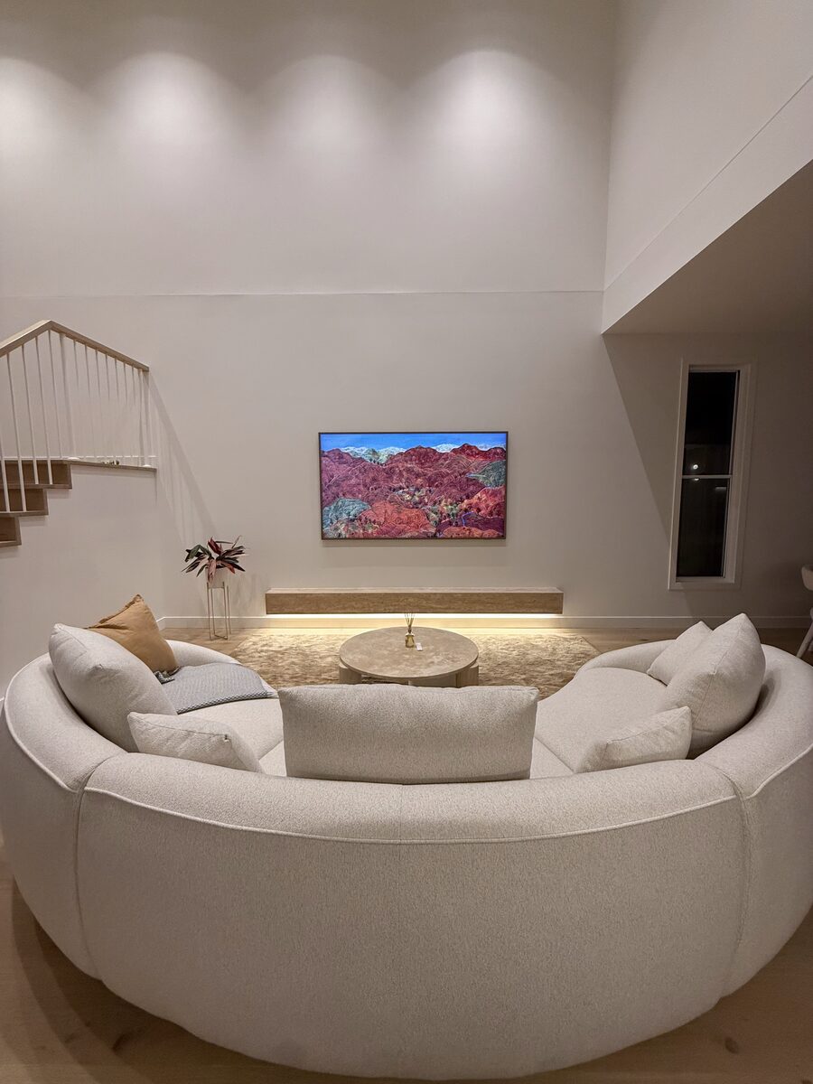 Samsung Frame TV mounted on a double-height void wall, displaying a vivid red-rock mountain landscape in art mode, above a curved boucle sectional sofa.