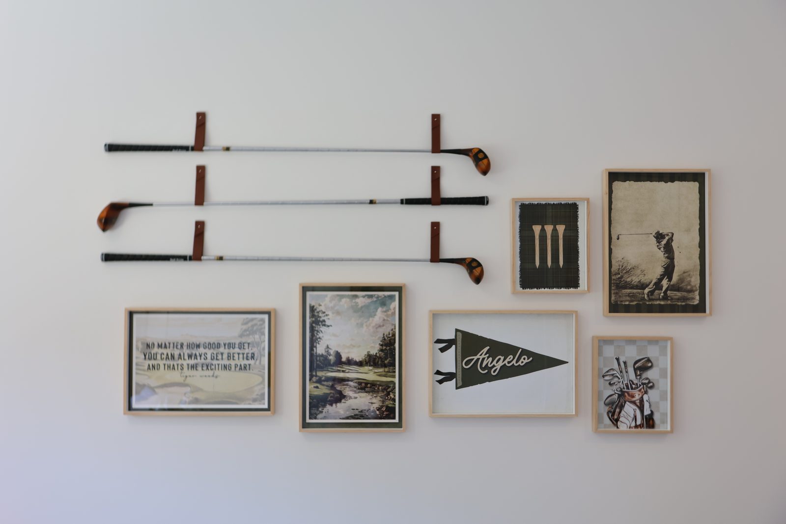 Salon-style gallery wall pairing vintage golf clubs on leather straps with six framed prints, a curated multi-piece hang.