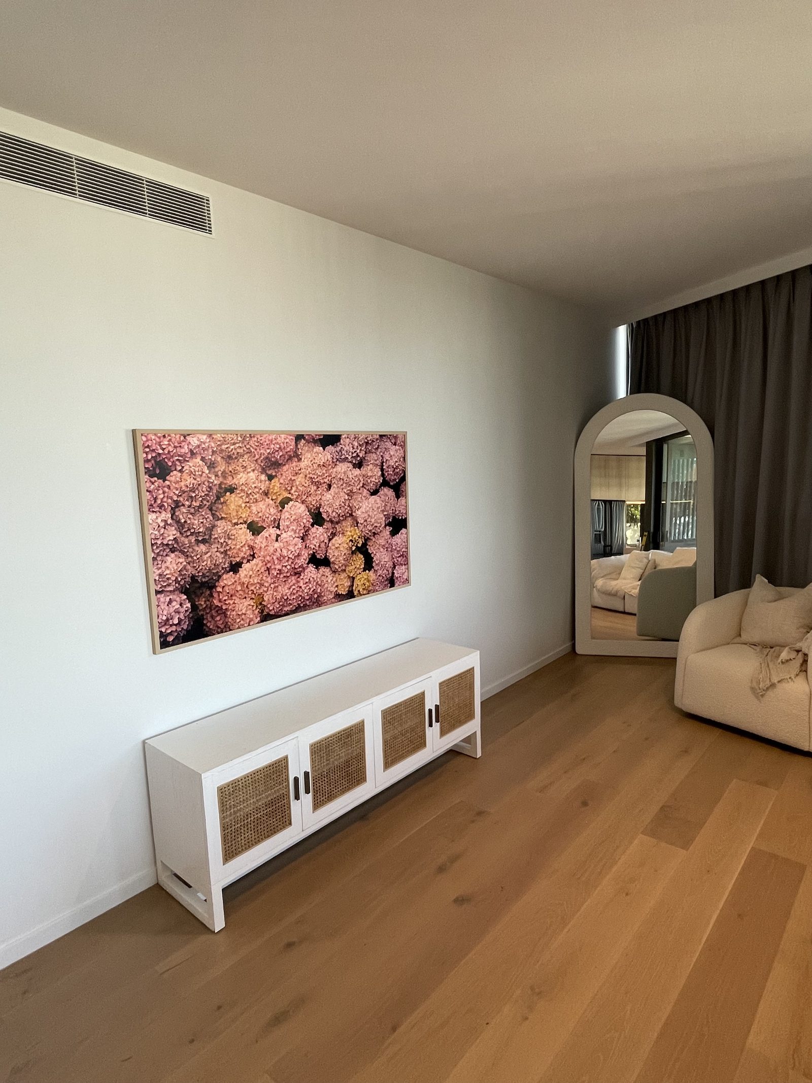 Large framed photographic print of pink hydrangeas hung above a white cane-fronted media unit, with a tall arched mirror to the right.