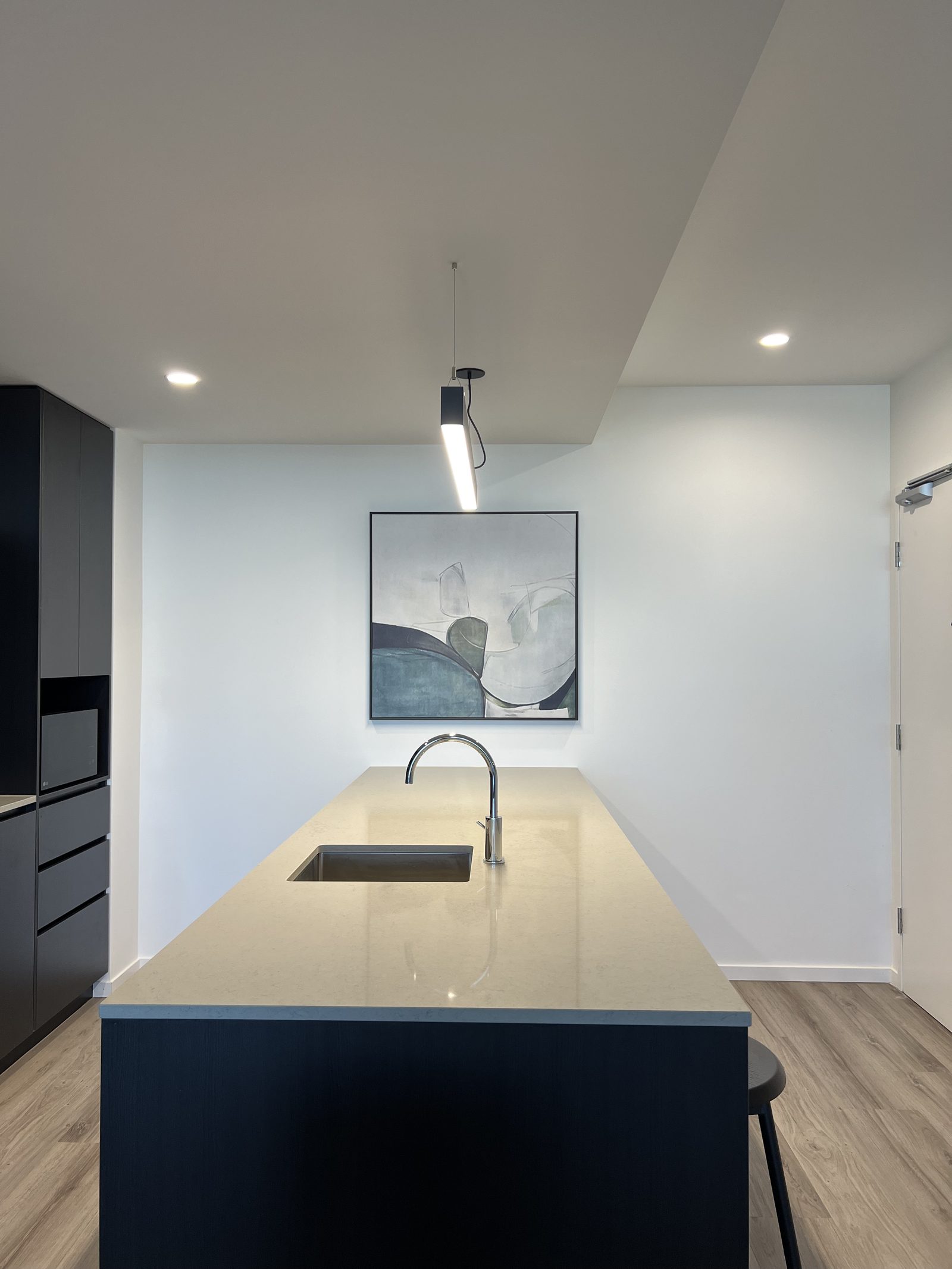 Large square abstract artwork hung centred on a kitchen wall above a stone island, lit by a black pendant light.