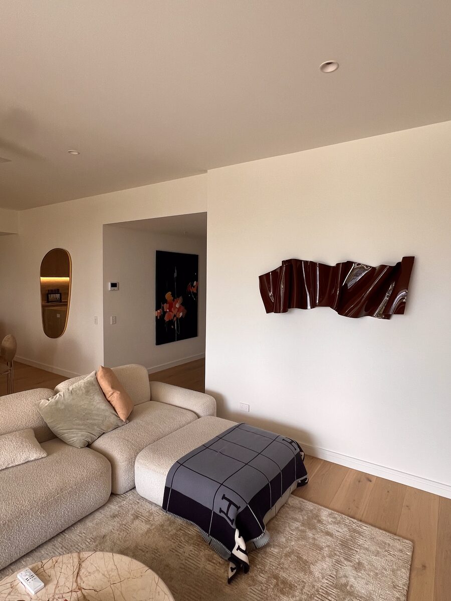 Glossy oxblood sculptural wall piece installed in a contemporary living room beside an arched mirror in the adjoining hallway.