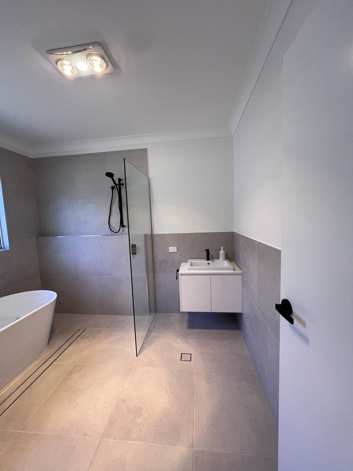 Bath, walk-in shower with black tapware and floating vanity, freshly finished bathroom.