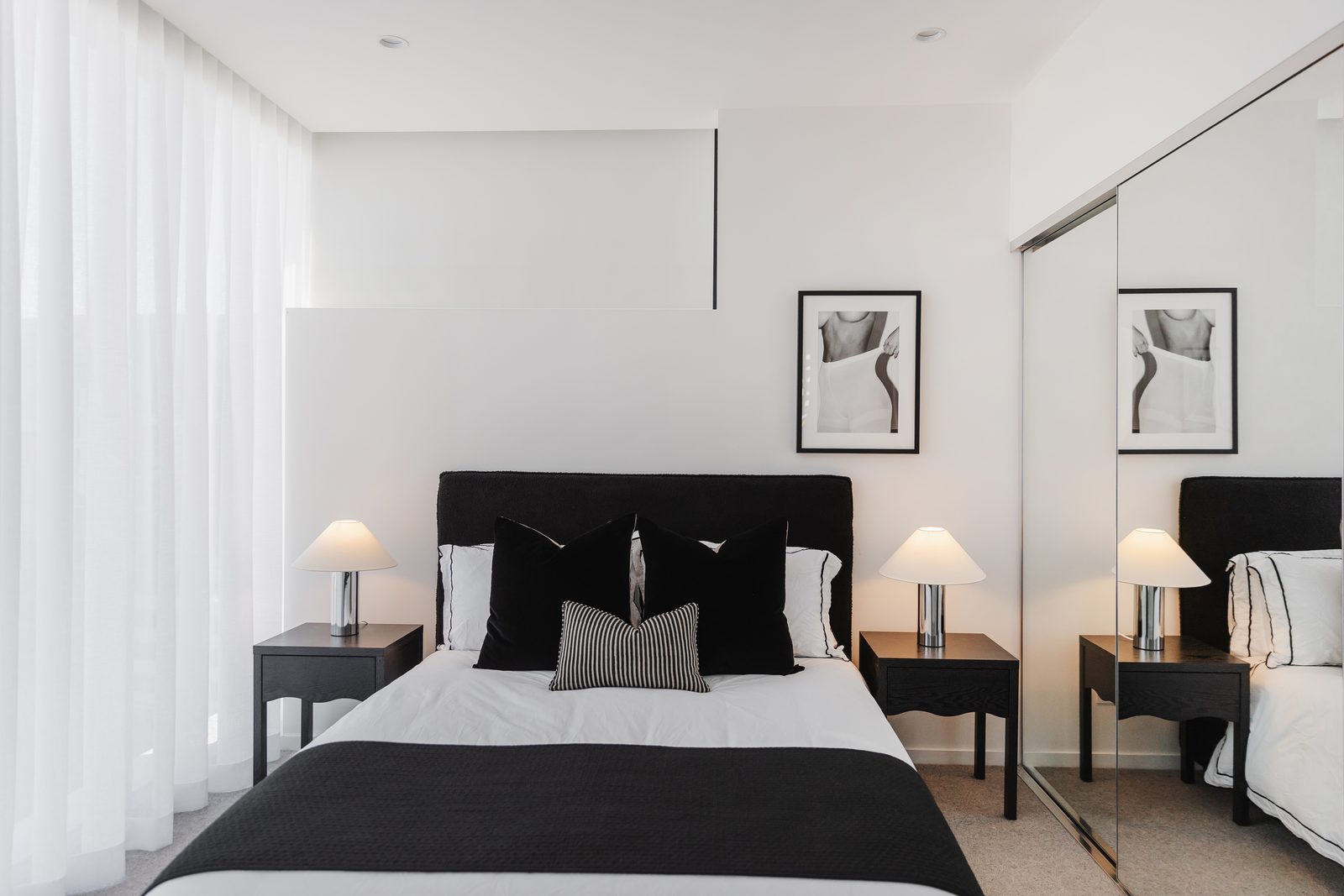 Black boucle upholstered bedhead fixed level above black bedside tables, with chrome lamps and a framed monochrome print above.