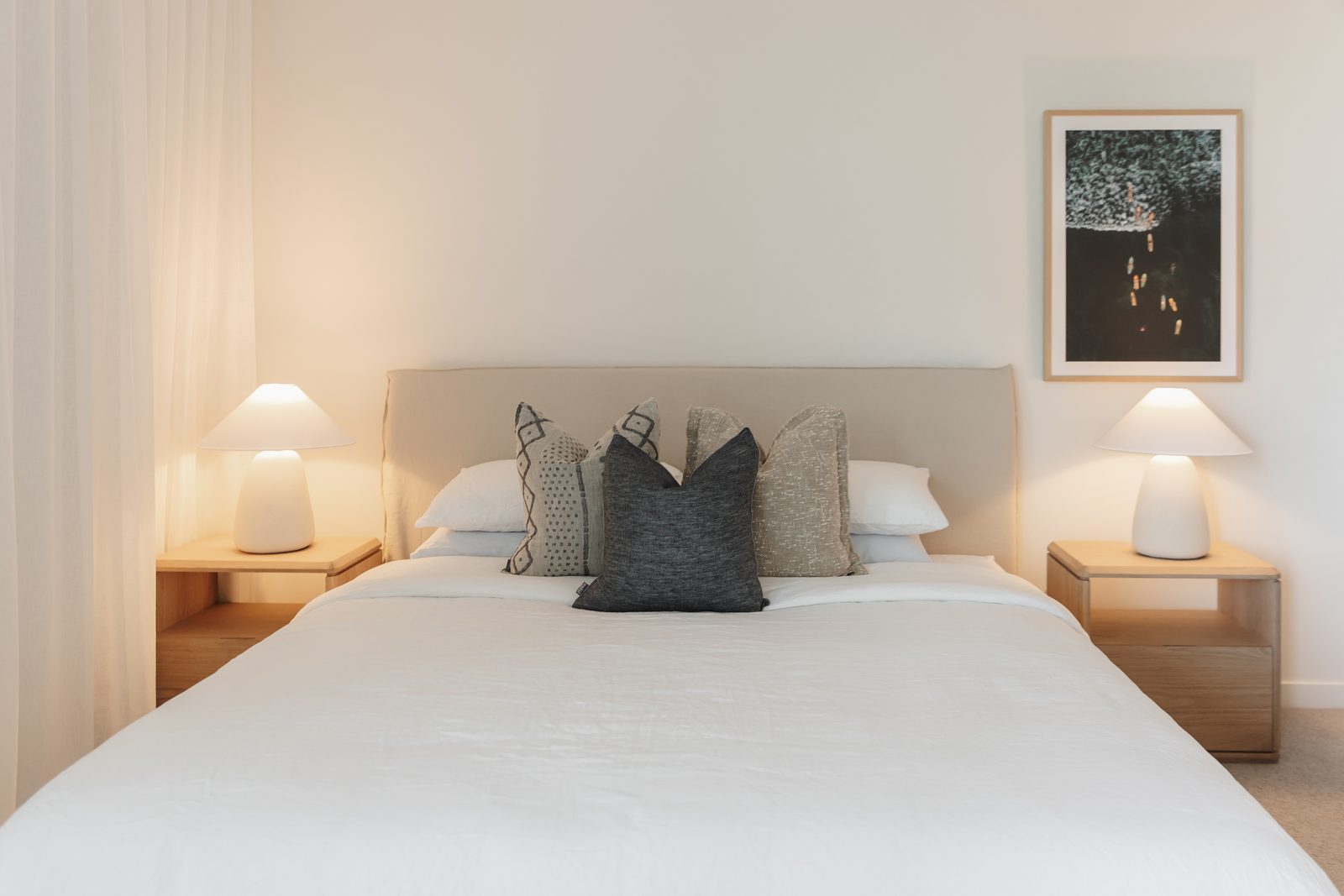 Cream linen upholstered bedhead mounted level on a master bedroom wall, with a framed abstract artwork hung to the right and mushroom-shade lamps either side. Cliff Hanger Installations.