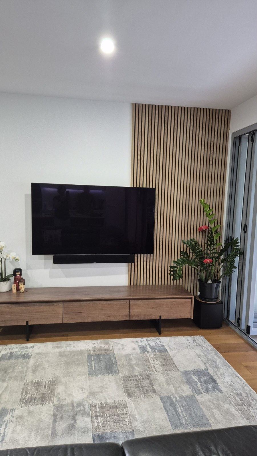 Floor-to-ceiling timber slat panel beside a wall-mounted TV in a lounge.