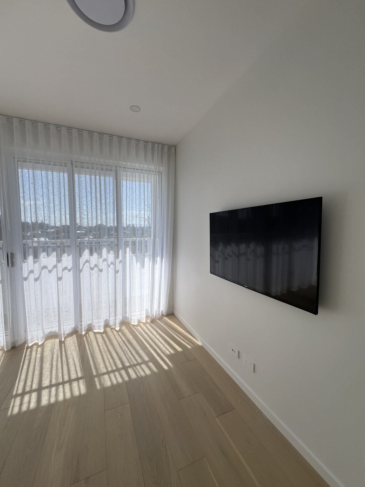 Clean TV install on a plain bedroom wall with sheer curtains, no visible cabling.