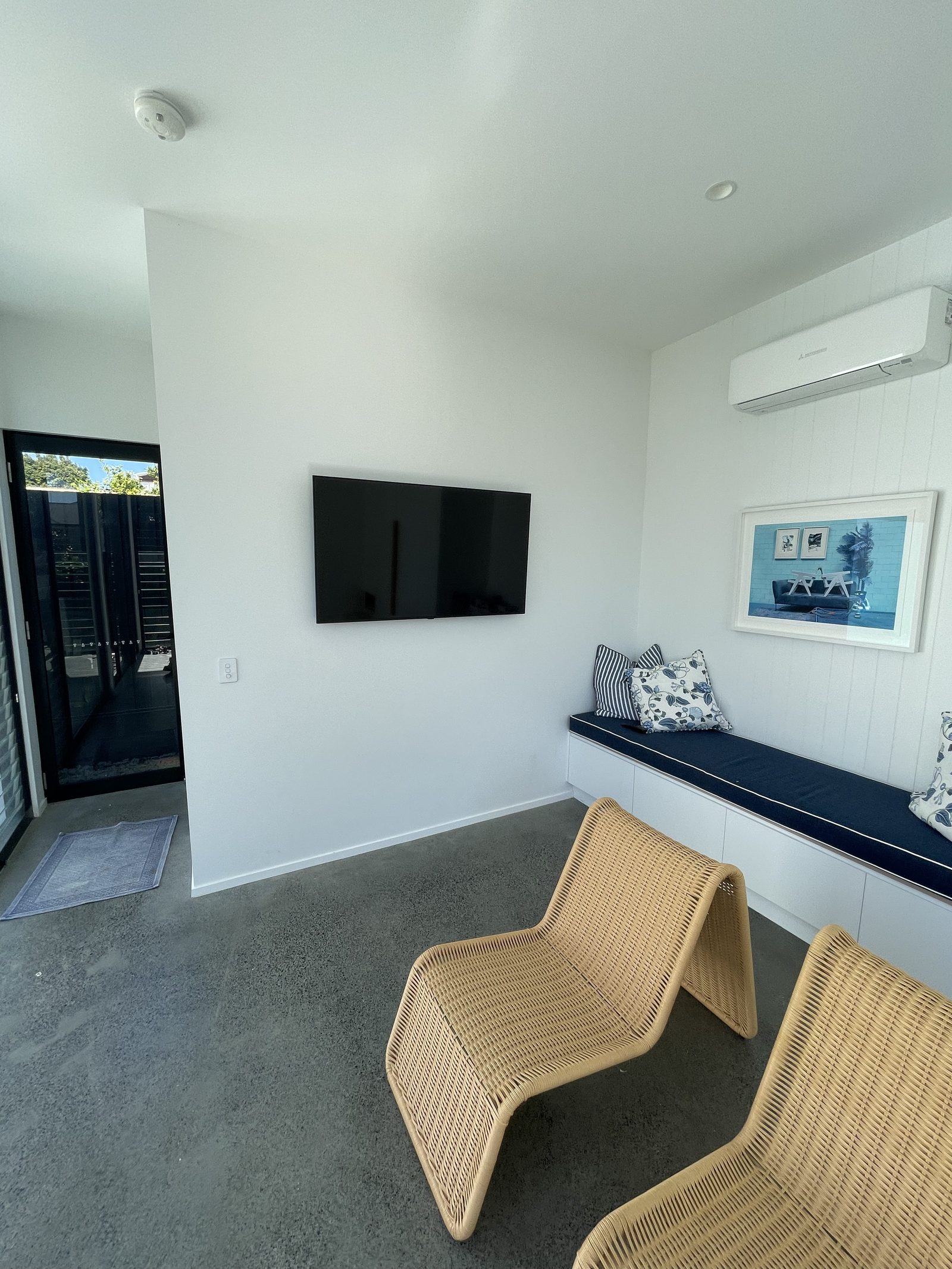 Wall-mounted TV in a poolside cabana lounge, with a framed photograph hung above a banquette bench and rattan loungers below.