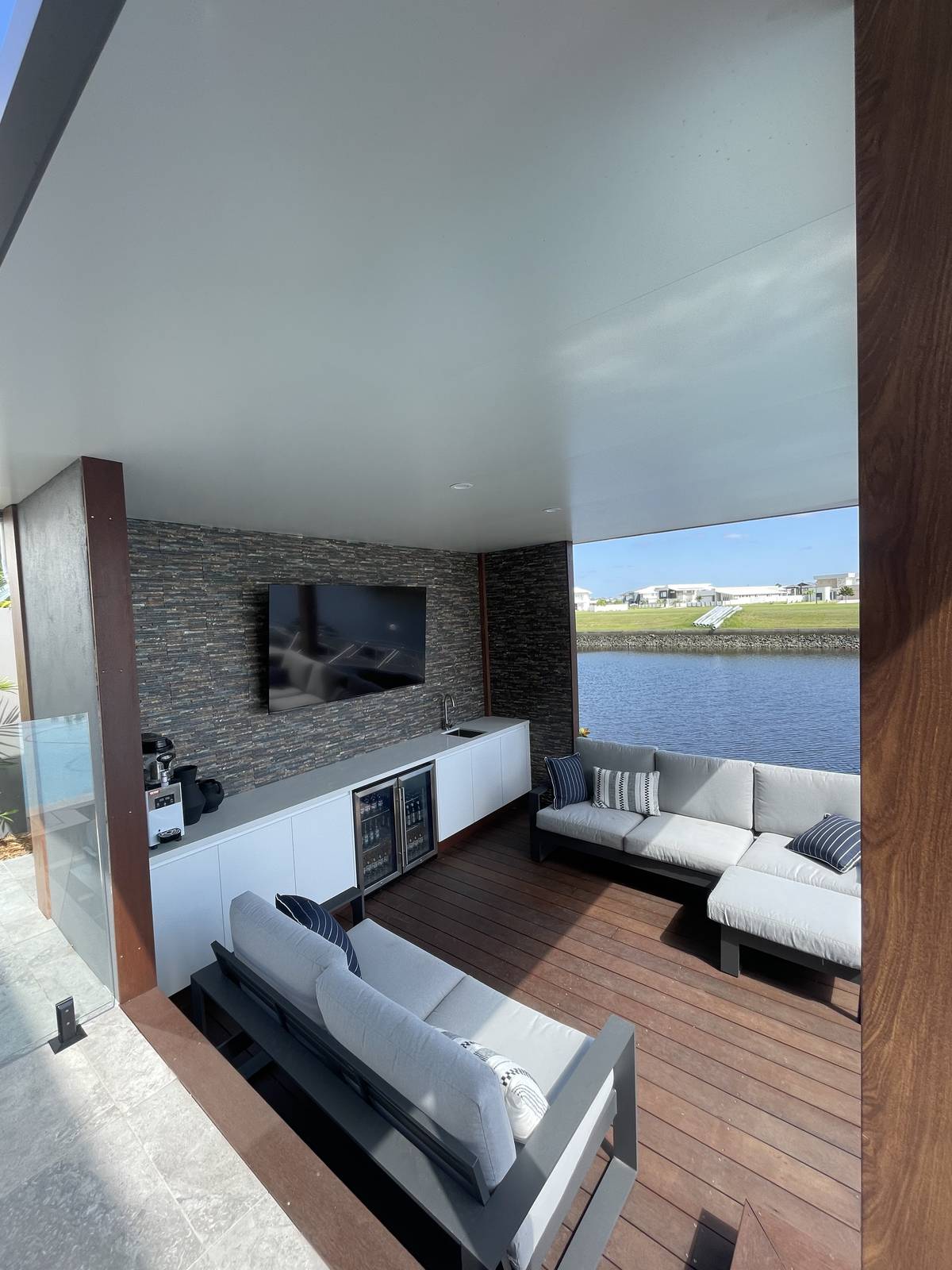 Wall-mounted TV on a stacked-stone feature wall in a Gold Coast canal-front alfresco lounge.