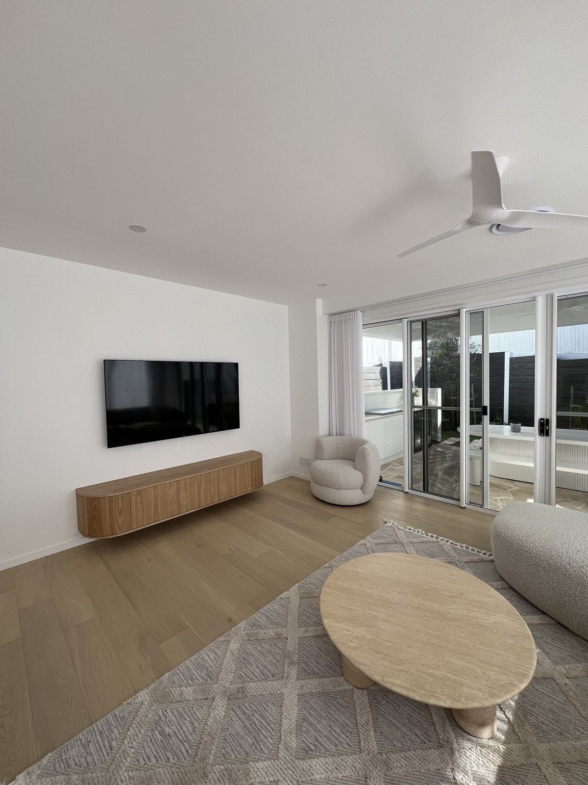 Wall-mounted TV above a light floating timber console in a modern lounge with views.