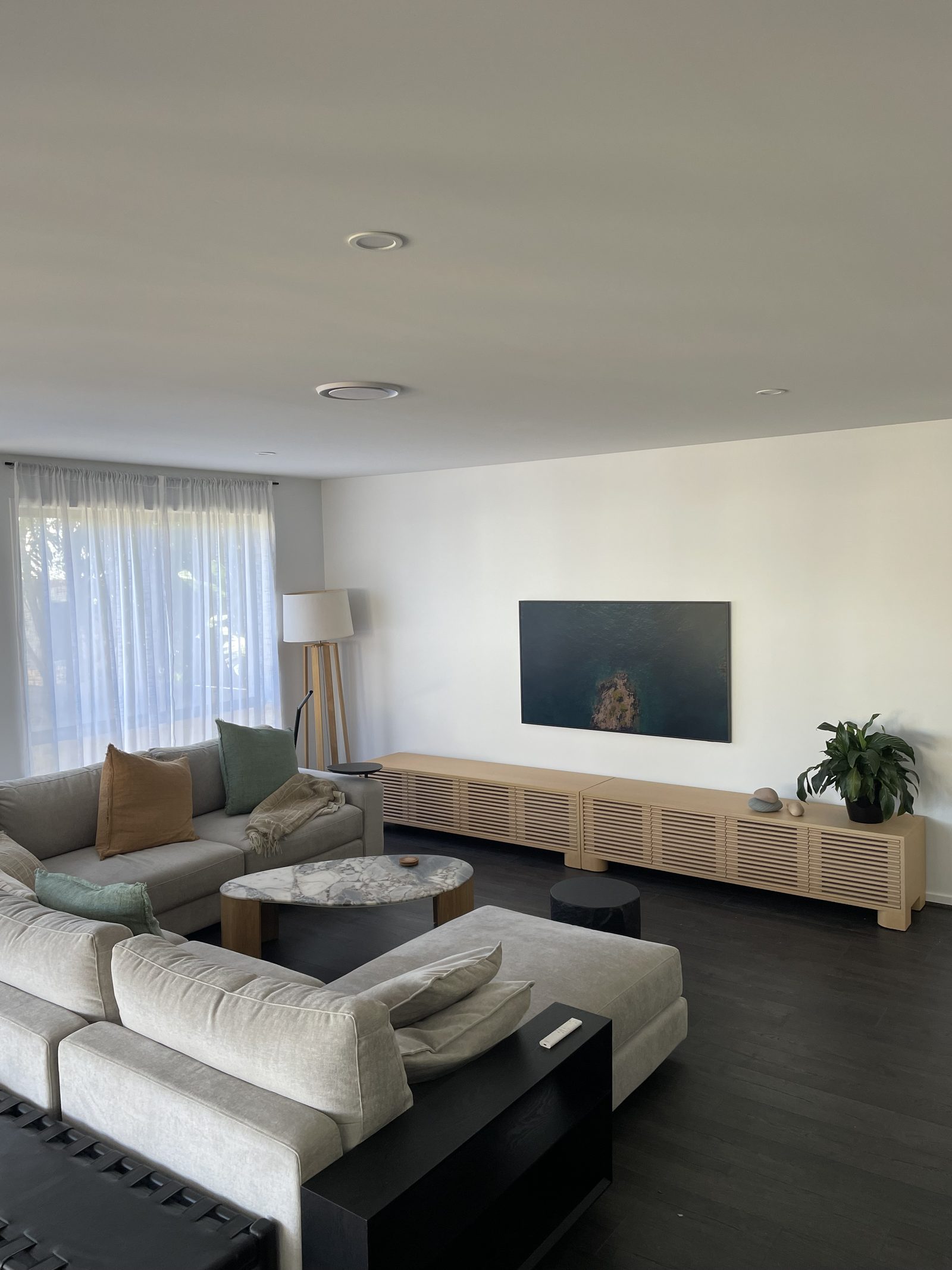 Wall-mounted TV alongside a large framed ocean artwork above a long timber slat media unit, set above a deep sectional lounge.