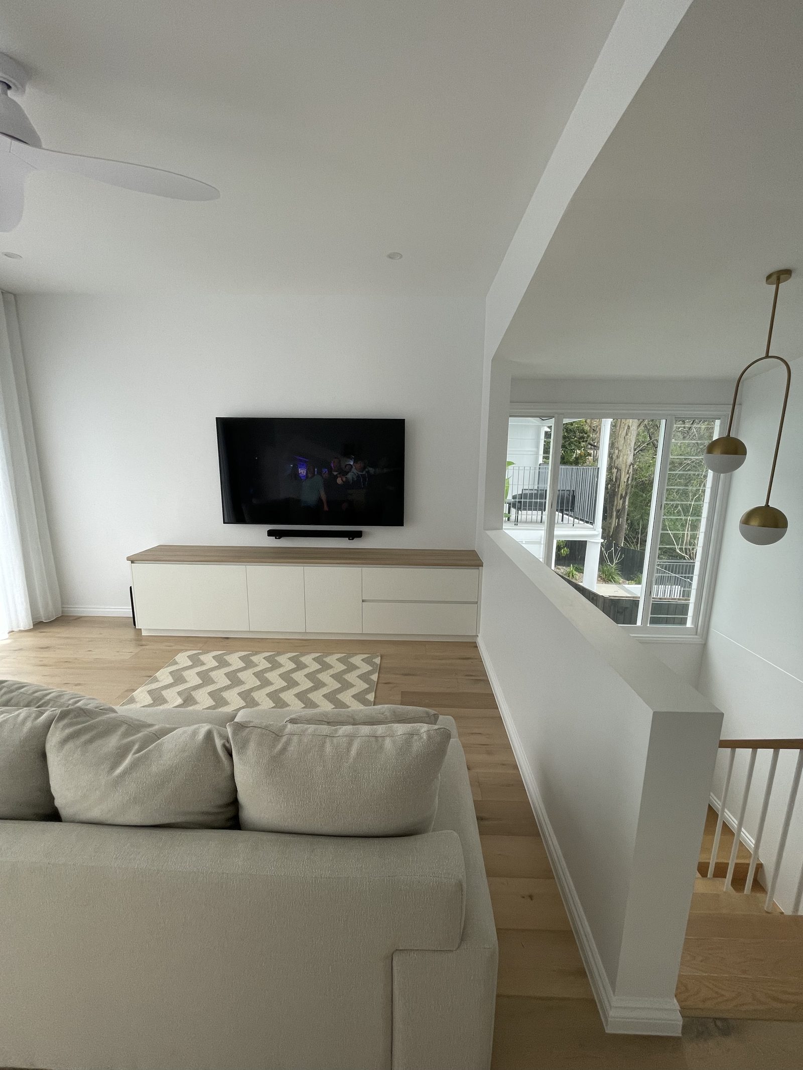 Wall-mounted TV with soundbar in an upstairs living room, set above a long white media console with a chevron rug below.
