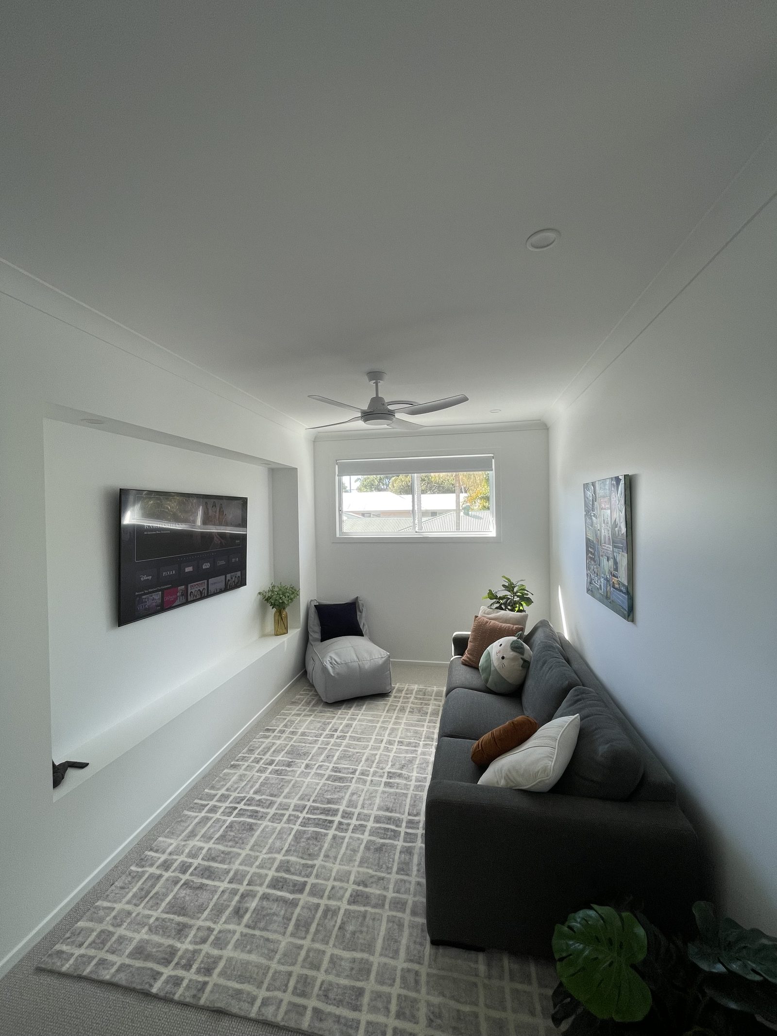 Wall-mounted TV in a long narrow media room with a built-in inset shelf below and framed artwork hung on the opposite wall.