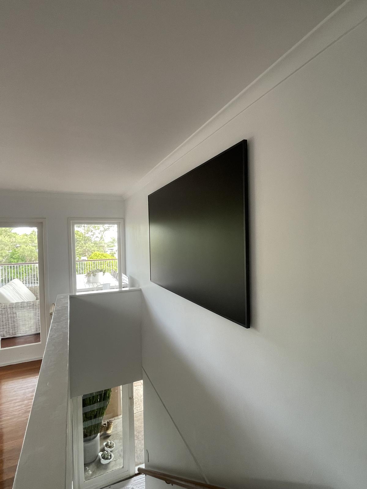Large flat-screen TV wall-mounted on a stairwell landing, set level on a clean white wall above an open void.