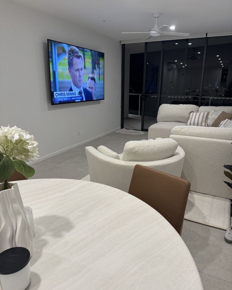 Wall-mounted TV in a Sunshine Coast apartment living room, clean install on a plain wall with balcony beyond.