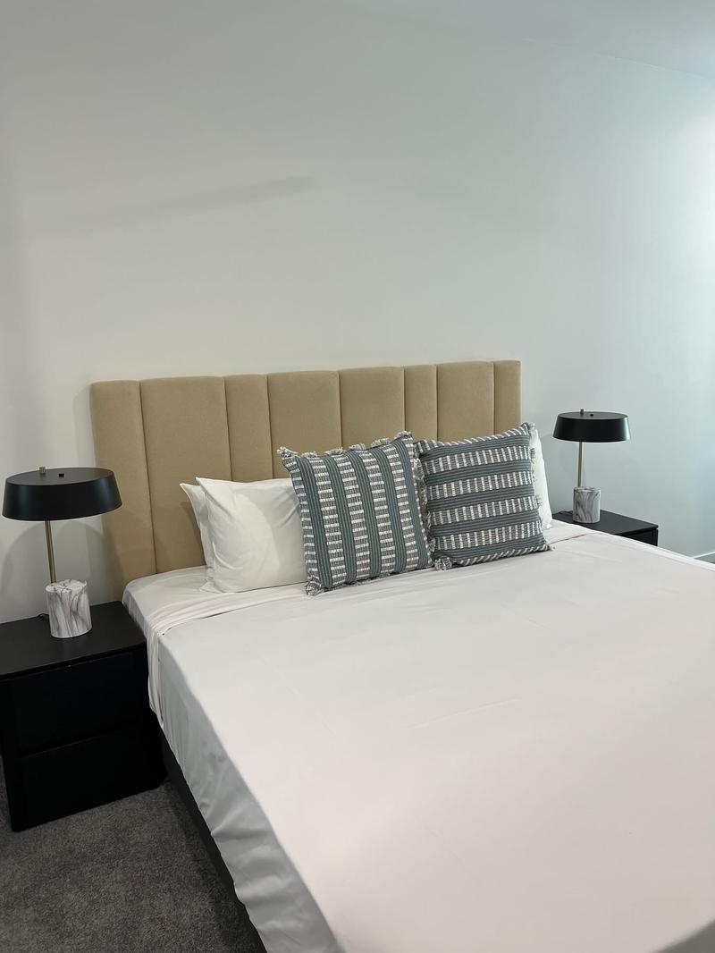 Upholstered bedhead fixed to a striped feature wall in a guest bedroom.