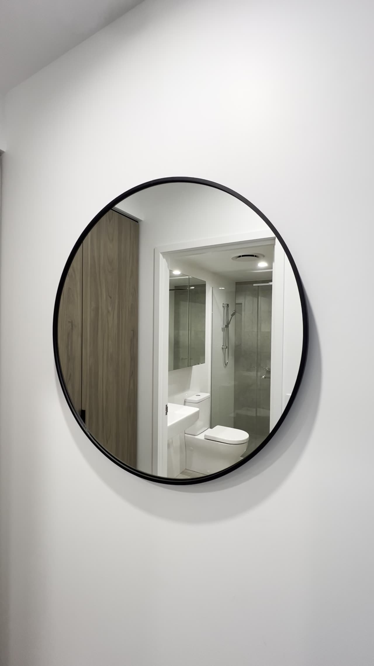 Round black-framed mirror installed in an entry hallway.